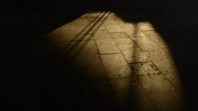 Luz dura cortando a sombra sobre uma superfície escura, em alto contraste de claro e escuro