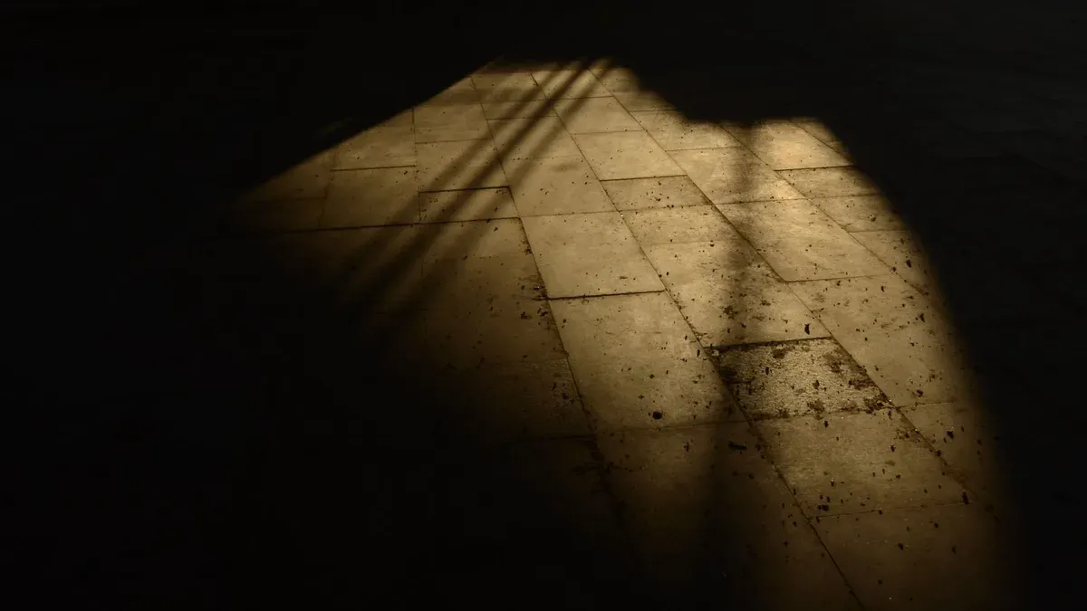 Luz dura cortando a sombra sobre uma superfície escura, em alto contraste de claro e escuro