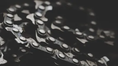 Elos de corrente de metal em close sobre fundo escuro, evocando a coleira e a guia do universo do pet play, sem pessoas no quadro