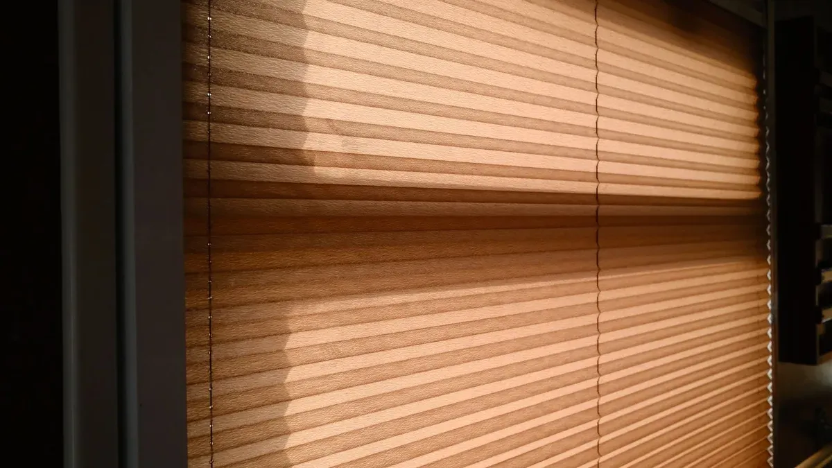 Luz e sombra de persianas entreabertas atravessando uma cortina, sugerindo o jogo entre olhar e ser visto