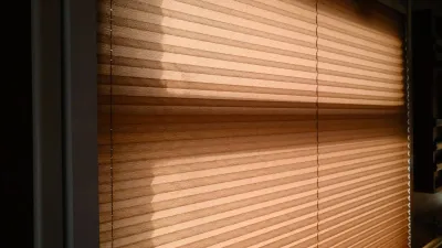 Luz e sombra de persianas entreabertas atravessando uma cortina, sugerindo o jogo entre olhar e ser visto